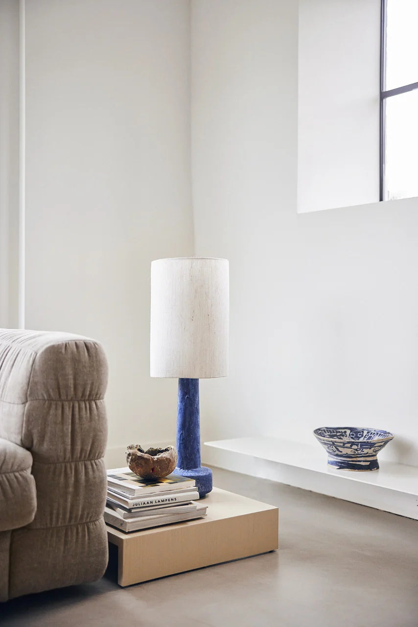 contemporary lava style lamp with blue base and white shade on a low wooden table next to a linen blend couch