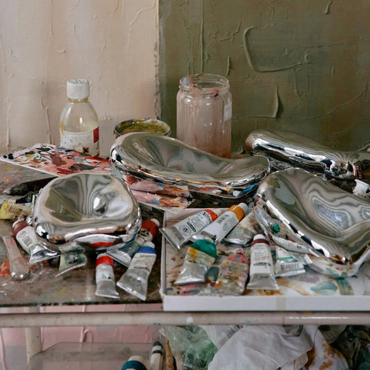 4 glass chrome colored bowls and paint, brushes and artist supplies on a table