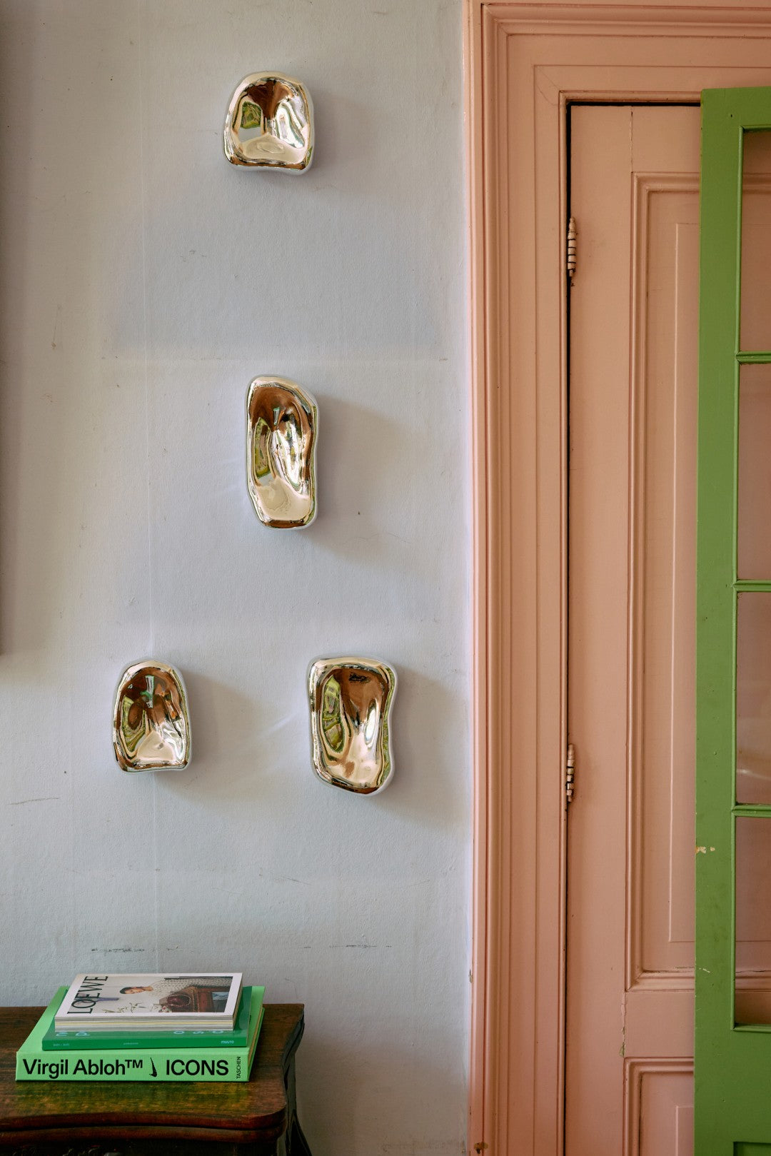 4 silver colored art objects hanging on a pale blue wall next to a pink door