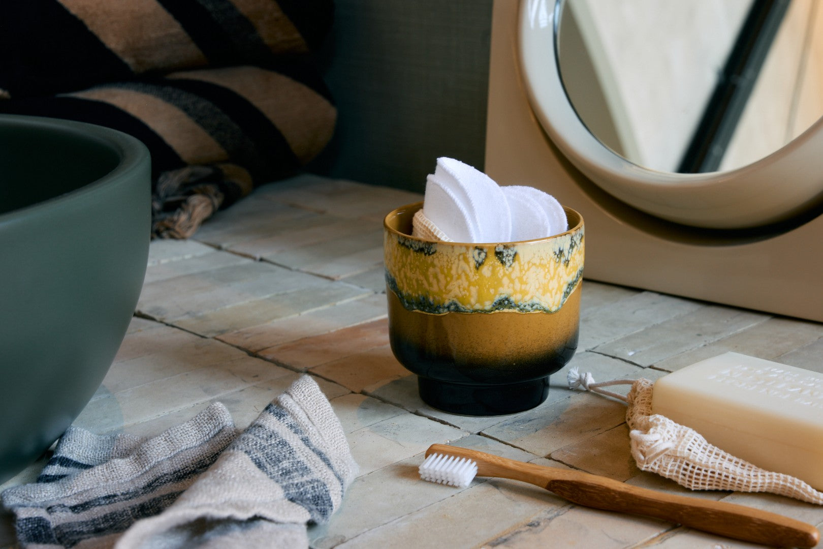 Ceramic cup with tissues on a bathroom counter next to a toothbrush and soap.