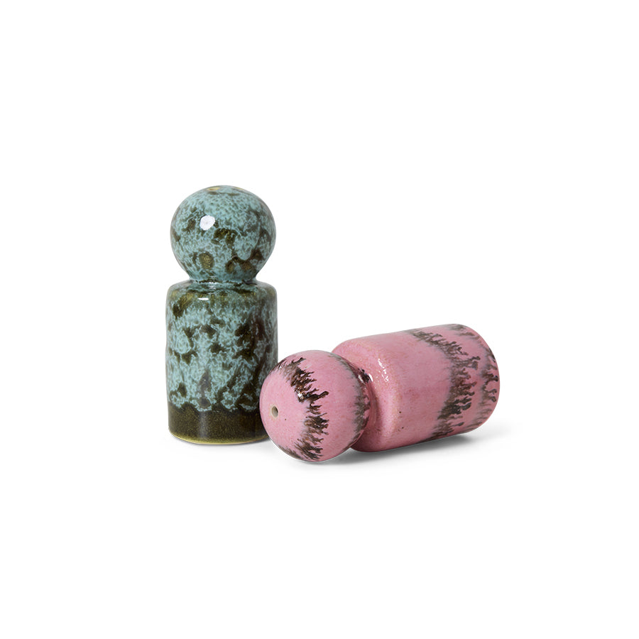 Two ceramic condiment shakers, one green and one pink, on a white background