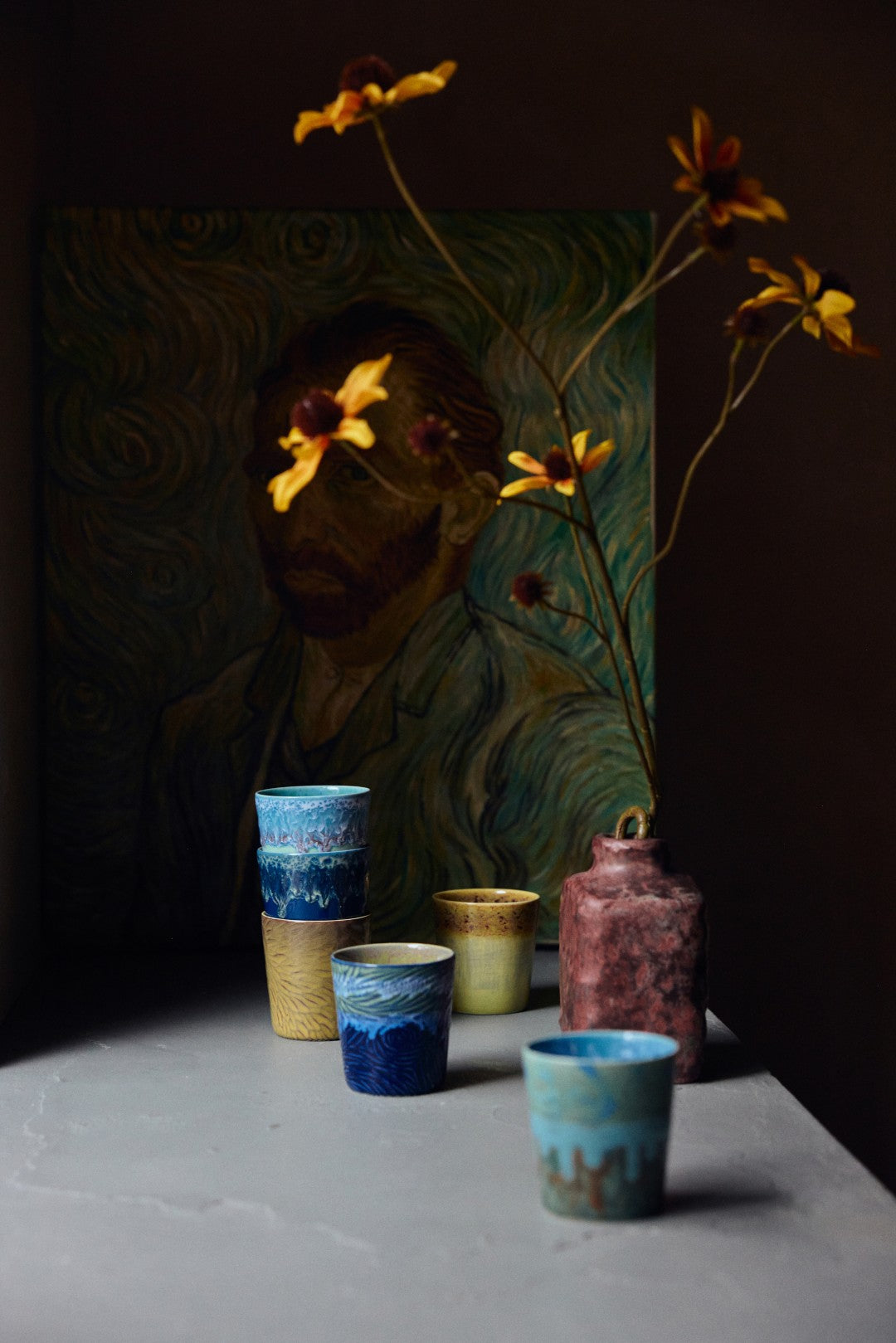 Collection of ceramic cups with a painting and flowers in the background