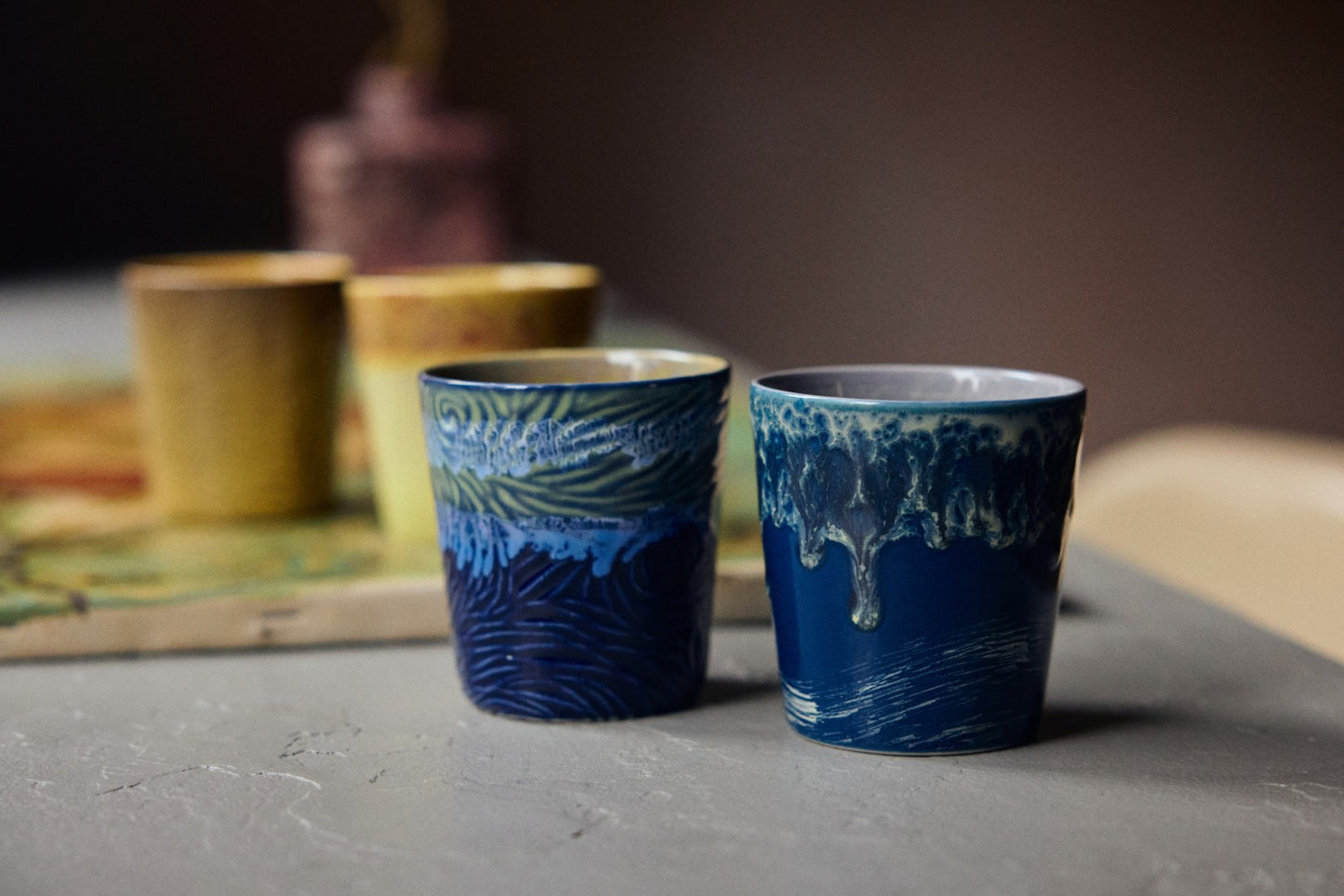 Two blue ceramic cups with textured design on a gray surface.