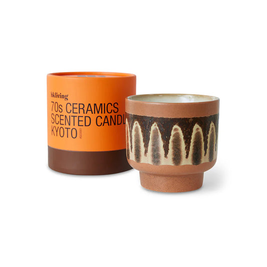 Ceramic candle with decorative pattern next to an orange label on a white background