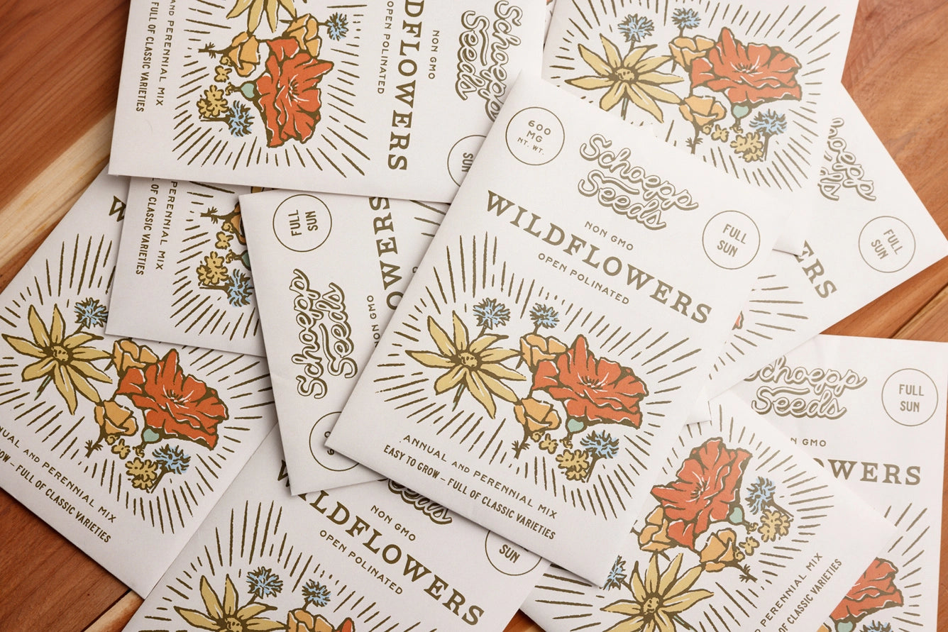 Seed packets with floral designs and text on a wooden surface