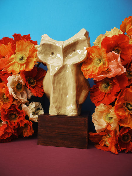 Decorative owl sculpture on a wooden base with orange and red flowers against a blue background