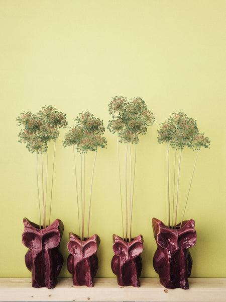 Four owl-shaped vases with plants on a light green background