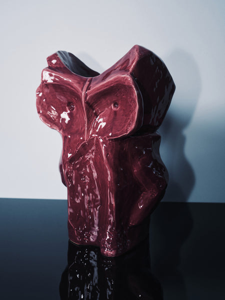 Maroon ceramic vase with a glossy finish on a reflective surface