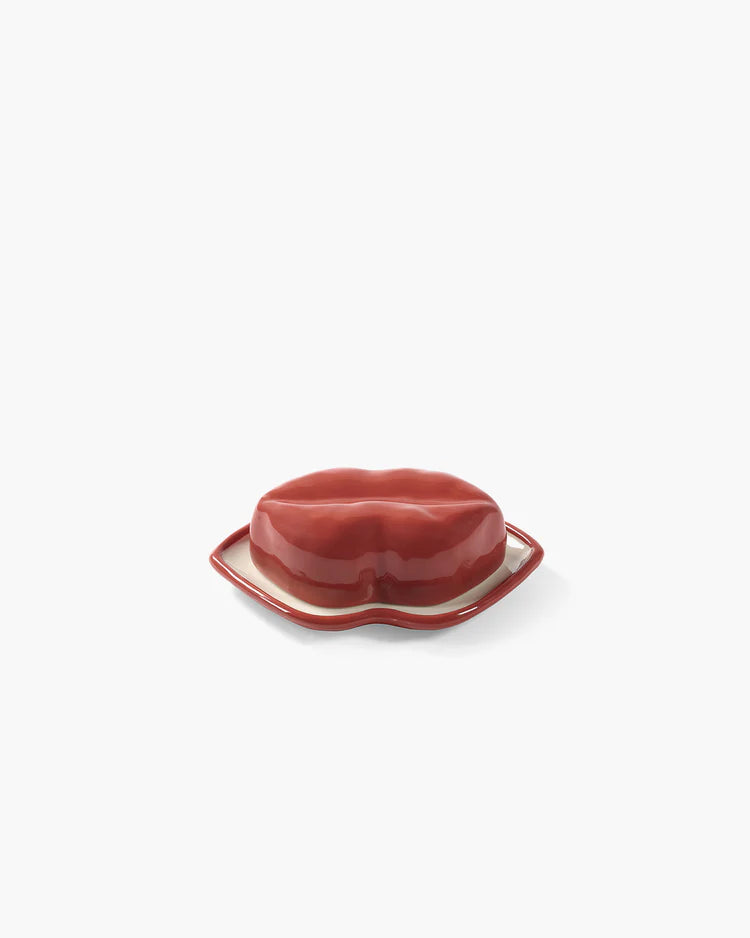 Red ceramic lips-shaped object on a white plate against a white background