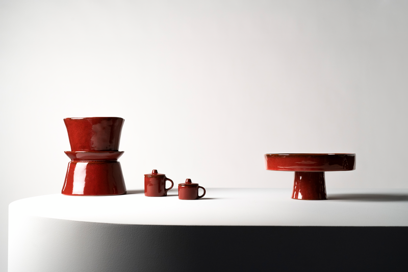 Set of red ceramic items including a pot, mug, and small container on a white surface with a light gray background.