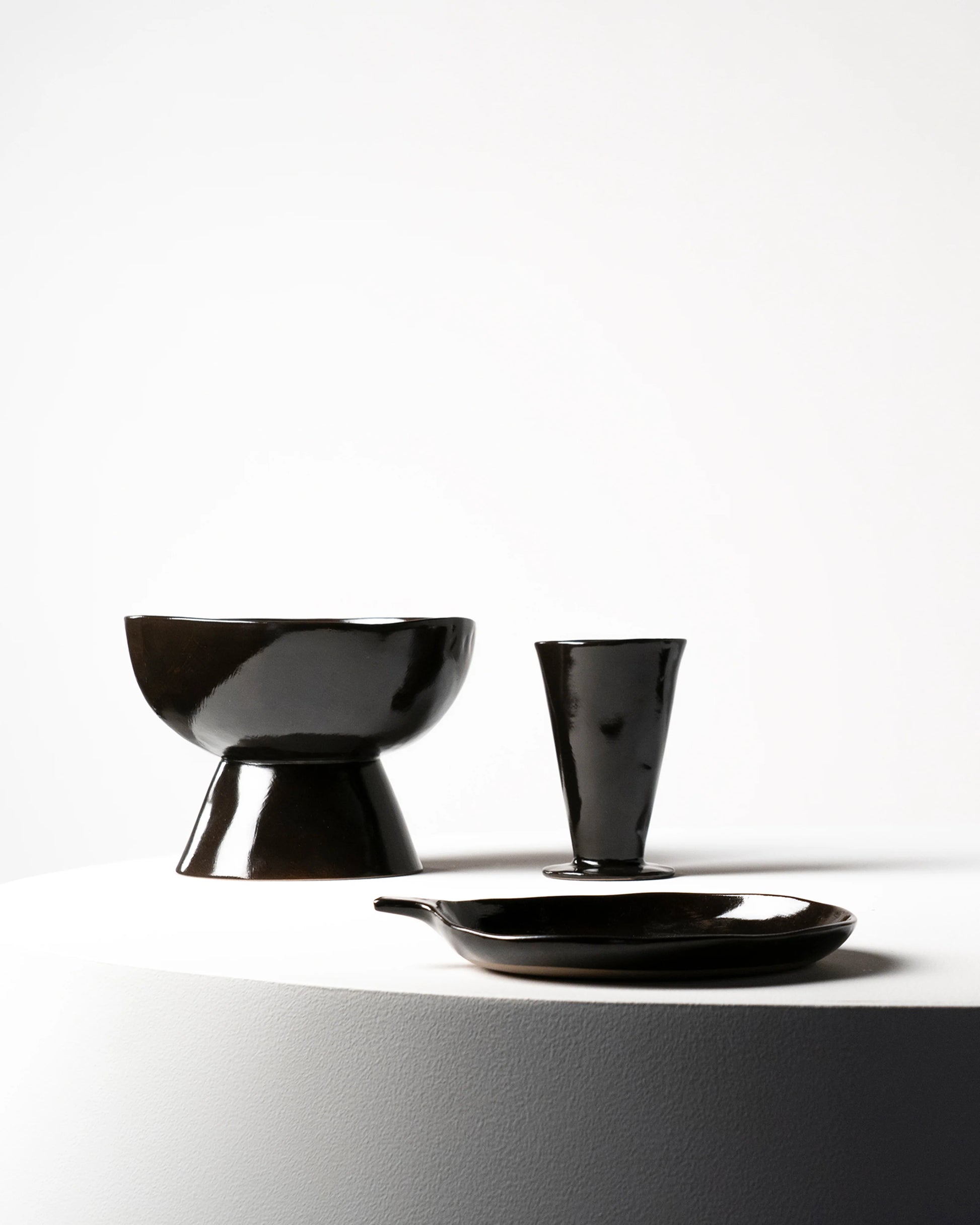 Black ceramic tableware including a bowl, cup, and plate on a white background
