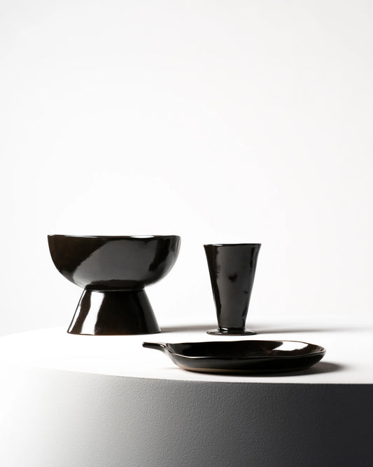 Black ceramic tableware including a bowl, cup, and plate on a white background