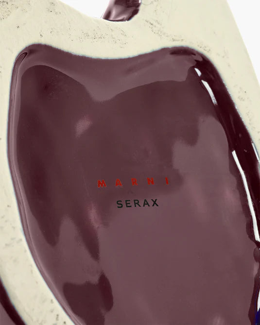 Close-up of a dark red or burgundy product with 'Marni' and 'Serax' branding on a beige background.