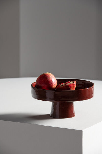 Red ceramic pedestal dish with pomegranate on a white surface