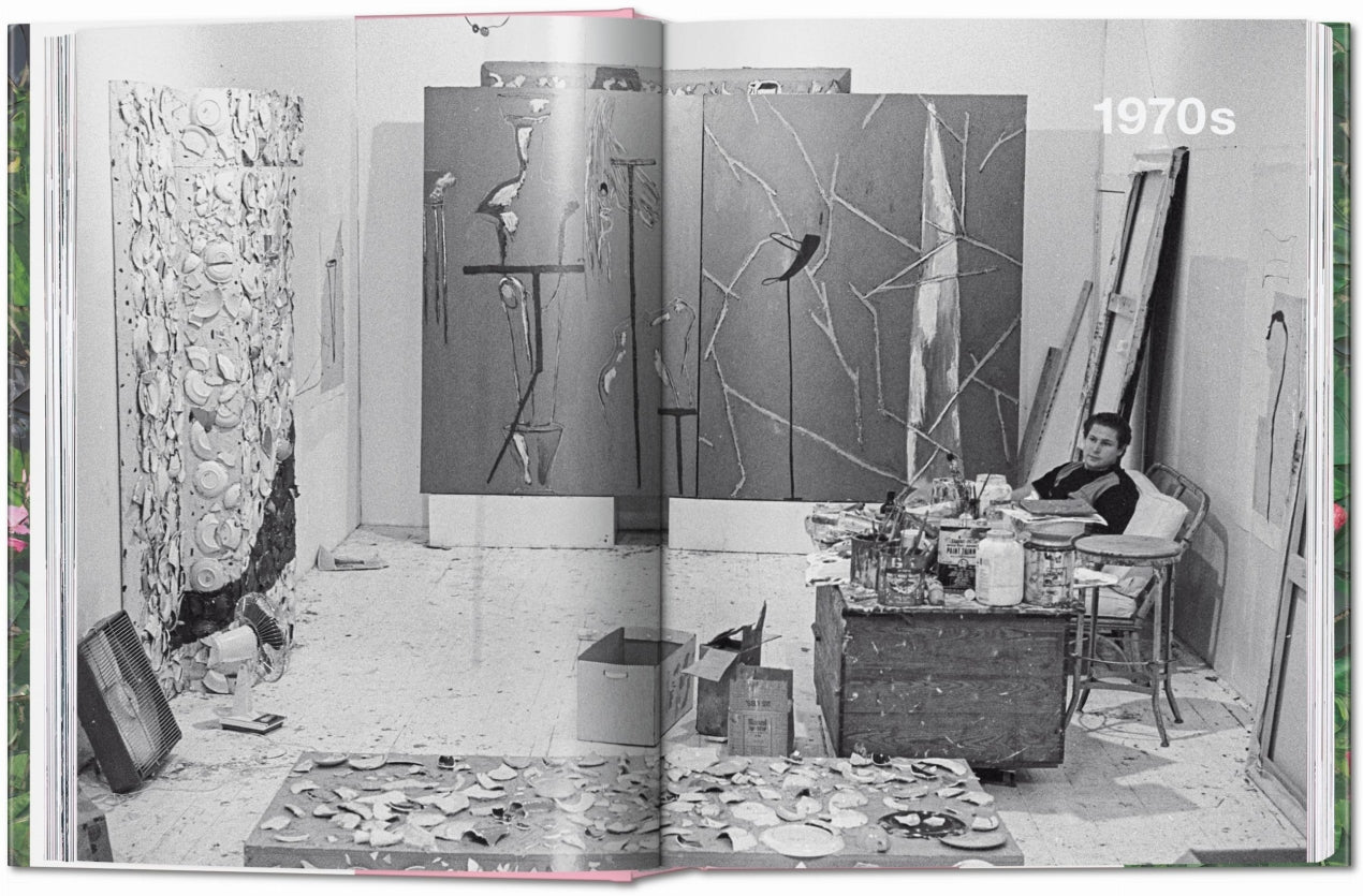 Page from a book showing a black and white photograph of a room with art pieces and a person sitting on a chair.