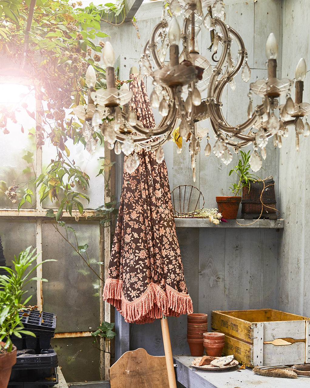 retro style beach umbrella with brown and orange floral fabric and orange fringes in a shed leaning aganst a wall with a vintage chandelier hanging in front of it