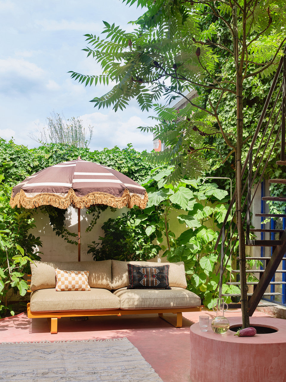 brown and cream graphic design parasol with wooden pole and golden fringes and orange outdoor sofa with beige cushions