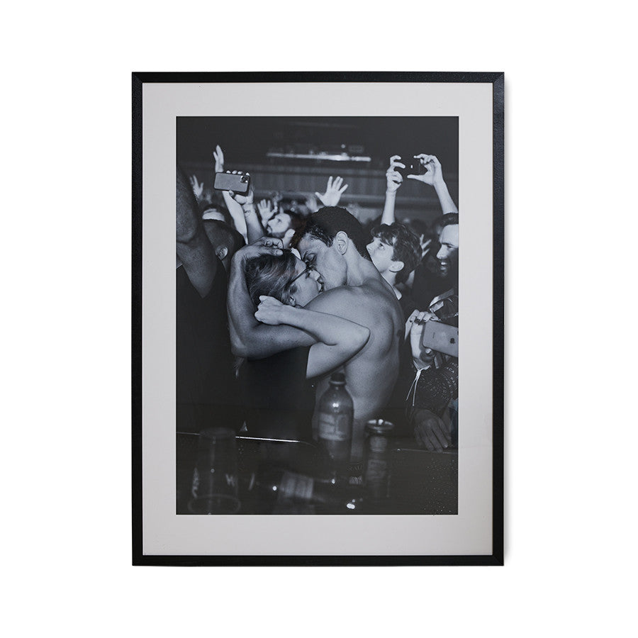 black and white photo of boy and girl kissing at festival, framed in black frame