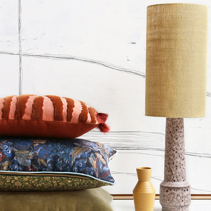 table lamp with linen shade and a stack of 3 different  accentpillows