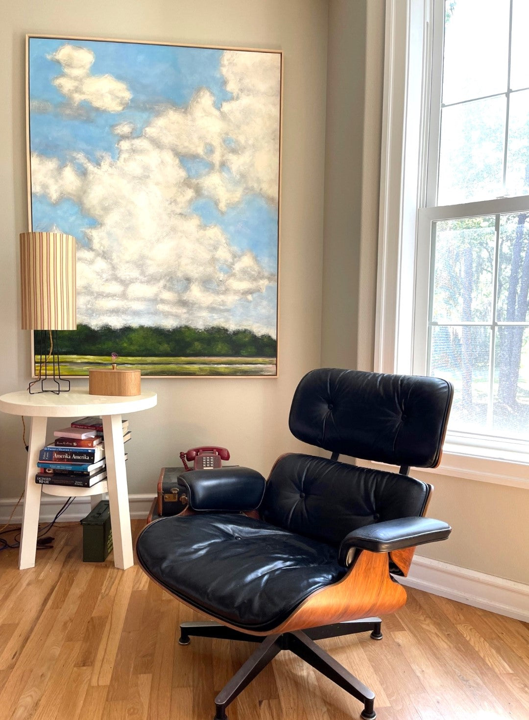striped table lamp on a black metal open base with golden cord in front of a large modern landscape painting with an Eames chair