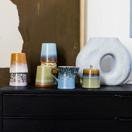 sculptural vase and ceramic coffee cups on top of a black drawer