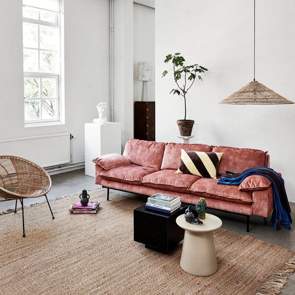 living room with pink retro style sofa wicker lamp and earthenware side table